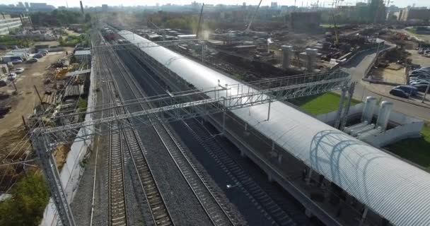 Electric train arriving to the station in city outskirts, aerial view — Stock Video