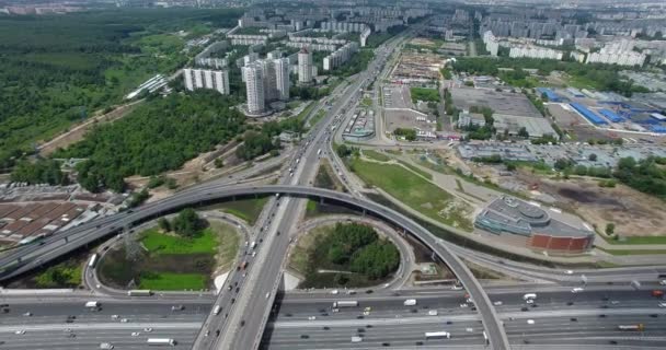 Een luchtfoto van een enorme en drukke wegkruising in het midden van het groene stedenlandschap — Stockvideo