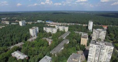 Yeşil ağaç taçlarında boğulan çok katlı binaların havadan görüntüsü.