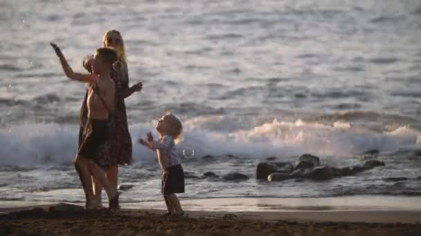 Mamá con niños juguetones en la playa de arena negra. Vacaciones familiares — Vídeos de Stock