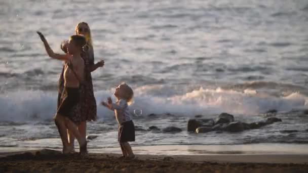 Mamma con bambini giocherelloni sulla spiaggia di sabbia nera. Vacanza in famiglia — Video Stock