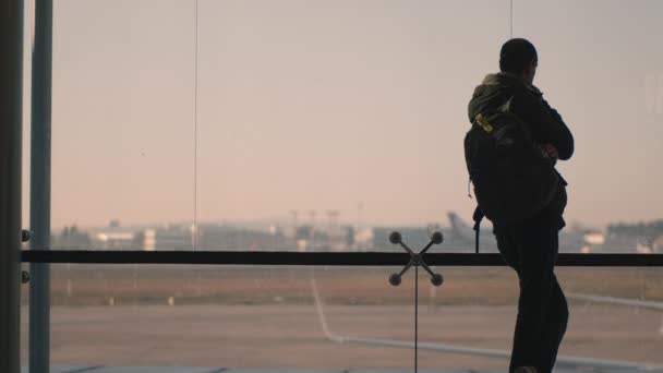 Sebuah backview dari seorang pria berdiri di samping jendela bandara besar — Stok Video
