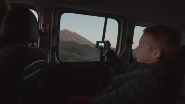 Ein Junge auf dem Rücksitz des fahrenden Autos fotografiert die Berglandschaft — Stockvideo