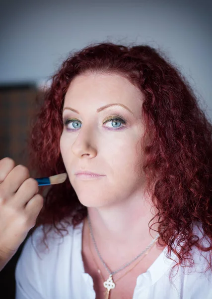 Рыжеволосая милая девушка в парикмахерской делает профессиональный макияж — стоковое фото