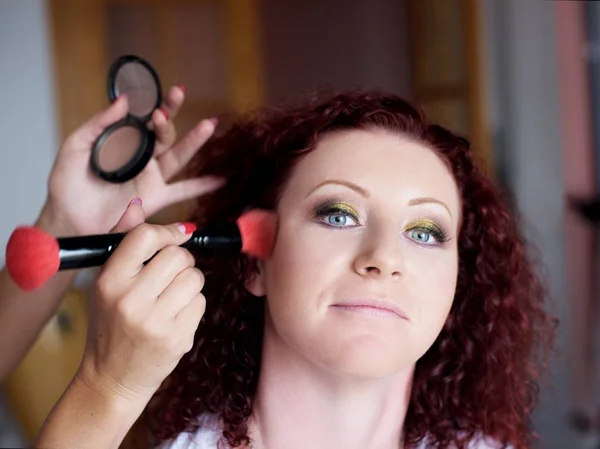 Menina linda de cabelos vermelhos em um salão de cabeleireiro faz maquiagem profissional — Fotografia de Stock