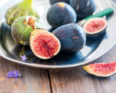 Bütün ve dilimlenmiş incir bir tabak ve ahşap bir masa. Güzel natürmort.