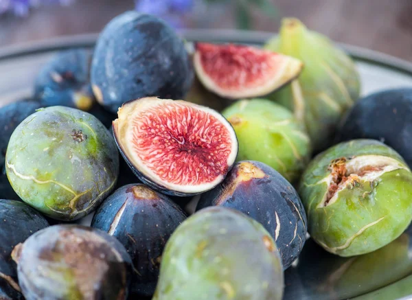 Whole and sliced figs on a plate and on a wooden table. Beautiful still life. — Stock Photo, Image