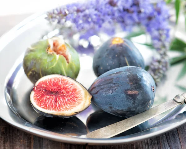 Bütün ve dilimlenmiş incir bir tabak ve ahşap bir masa. Güzel natürmort.