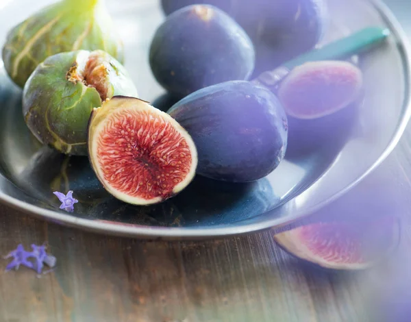 Bütün ve dilimlenmiş incir bir tabak ve ahşap bir masa. Güzel natürmort.