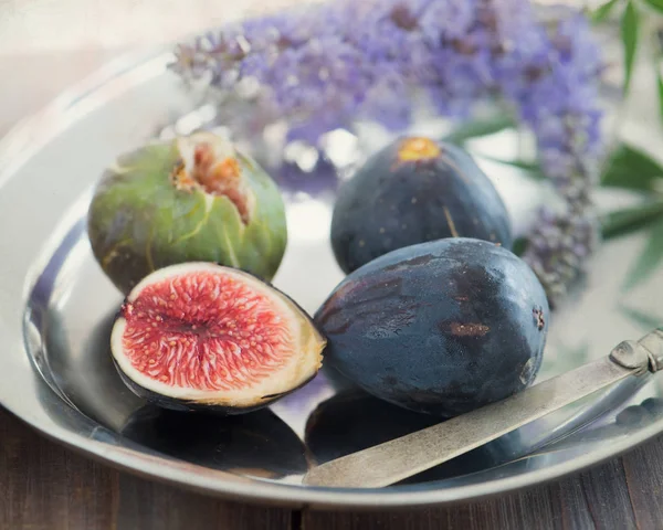 Bütün ve dilimlenmiş incir bir tabak ve ahşap bir masa. Güzel natürmort