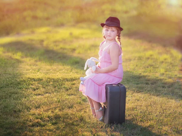 Menina em um chapéu senta-se em uma mala — Fotografia de Stock