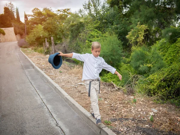 เด็กชายเดินไปตามขอบด้วยหมวกในมือของเขา . — ภาพถ่ายสต็อก