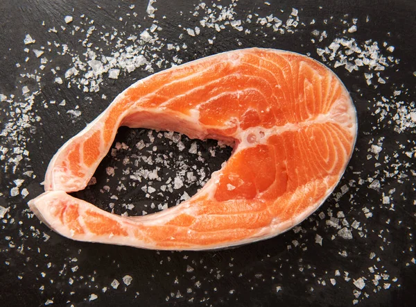 Fresh salmon steak with coarse salt on a black background. — Stock Photo, Image