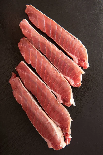 Slices of fresh tuna with coarse salt on a black background. — Stock Photo, Image