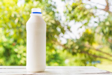 Süt şişesi beyaz ahşap masa üzerinde yeşil doğa bulanık arka plan.
