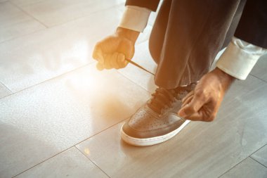 Bir adamın vücudunun bir parçasını işaret fişeğiyle yerde otururken bağcıklarını bağlamak için ellerini kullanan bir adam..