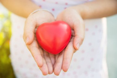 Kırmızı bir kalp şeklindeki topu beyaz desenli, arka planda bulanık bir elbiseyle kadın ellerine tak.. 