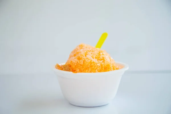 A sweet homemade shaved iced with orange syrup in a white foam bowl on white background.
