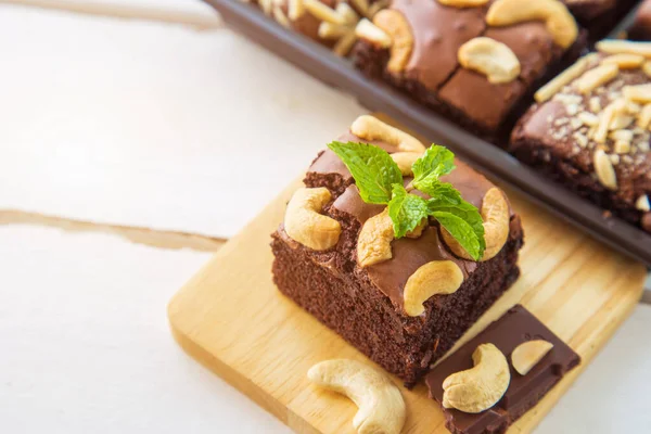 Close up chocolate brownies with cashew nut and peppermint on wooden plate on white wooden floor with brownies box blurred background.