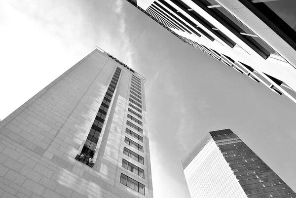 Perspective and underside angle view to textured background of modern glass building skyscrapers over blue cloudy sky. Black and white