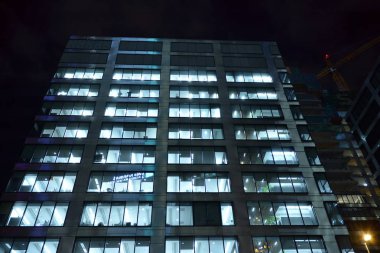 Ofis binalarının pencereleri gece aydınlandı. Şehir merkezinde yansıması olan cam mimari cephe tasarımı ile ışıklandırma.