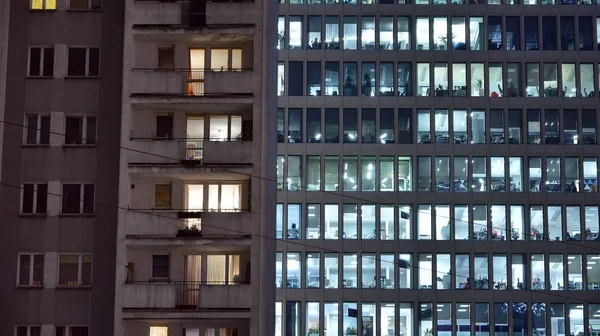 Pattern of office buildings windows illuminated at night adjacent to an old residential building. Lighting with Glass architecture facade design with reflection in urban city.