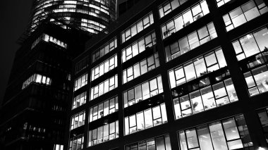Ofis binalarının pencereleri gece aydınlandı. Şehir merkezinde yansımalı cam mimari ön cephe tasarımı ile aydınlatma. Siyah ve beyaz.