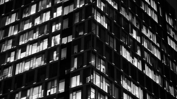 Pattern of office buildings windows illuminated at night. Lighting with Glass architecture facade design with reflection in urban city. Black and white.
