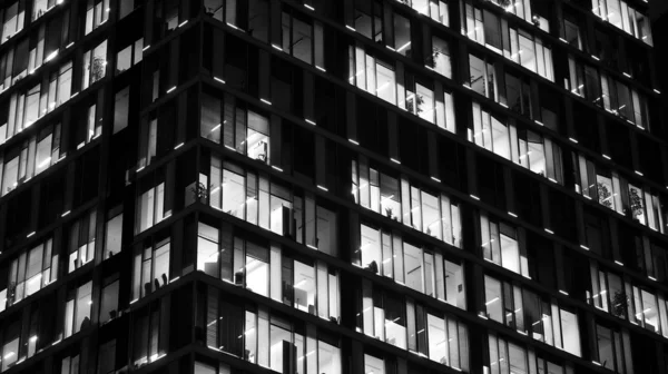 Pattern of office buildings windows illuminated at night. Lighting with Glass architecture facade design with reflection in urban city. Black and white.