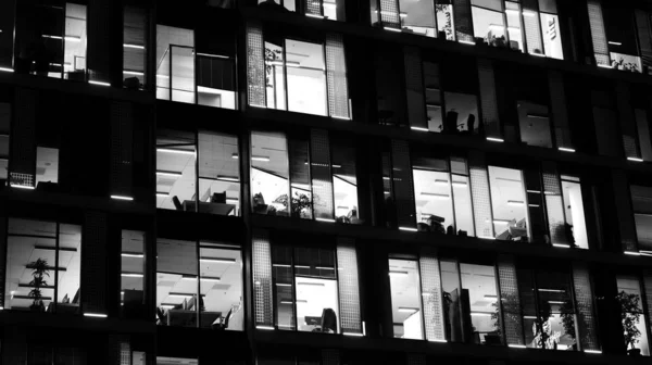 Pattern of office buildings windows illuminated at night. Lighting with Glass architecture facade design with reflection in urban city. Black and white.