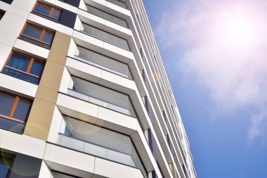 Mavi gökyüzü olan güneşli bir günde modern apartman binaları. Modern bir apartmanın ön cephesi. Güneş ışığıyla kaplı cam yüzey..