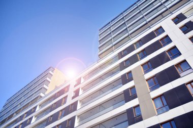 Mavi gökyüzü olan güneşli bir günde modern apartman binaları. Modern bir apartmanın ön cephesi. Güneş ışığıyla kaplı cam yüzey..