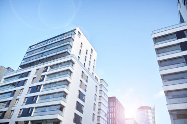 Mavi gökyüzü olan güneşli bir günde modern apartman binaları. Modern bir apartmanın ön cephesi. Güneş ışığıyla kaplı cam yüzey..