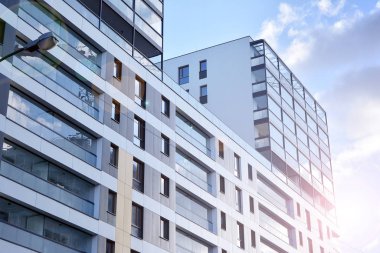 Mavi gökyüzü olan güneşli bir günde modern apartman binaları. Modern bir apartmanın ön cephesi. Güneş ışığıyla kaplı cam yüzey..