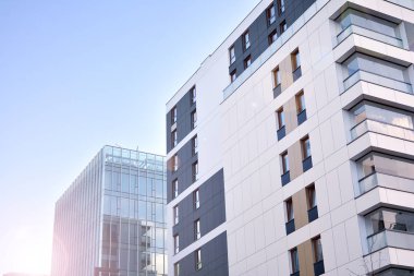 Mavi gökyüzü olan güneşli bir günde modern apartman binaları. Modern bir apartmanın ön cephesi. Güneş ışığıyla kaplı cam yüzey..