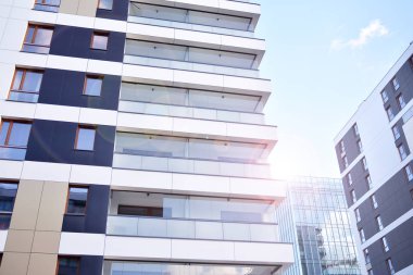 Mavi gökyüzü olan güneşli bir günde modern apartman binaları. Modern bir apartmanın ön cephesi. Güneş ışığıyla kaplı cam yüzey..
