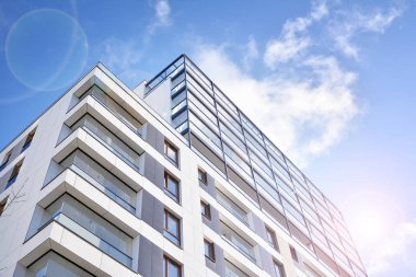Mavi gökyüzü olan güneşli bir günde modern apartman binaları. Modern bir apartmanın ön cephesi. Güneş ışığıyla kaplı cam yüzey..