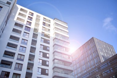 Mavi gökyüzü olan güneşli bir günde modern apartman binaları. Modern bir apartmanın ön cephesi. Güneş ışığıyla kaplı cam yüzey..