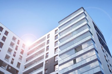 Mavi gökyüzü olan güneşli bir günde modern apartman binaları. Modern bir apartmanın ön cephesi. Güneş ışığıyla kaplı cam yüzey..