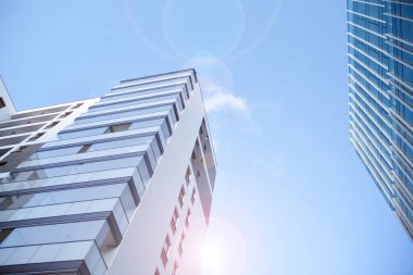 Mavi gökyüzü olan güneşli bir günde modern apartman binaları. Modern bir apartmanın ön cephesi. Güneş ışığıyla kaplı cam yüzey..