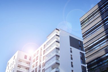 Mavi gökyüzü olan güneşli bir günde modern apartman binaları. Modern bir apartmanın ön cephesi. Güneş ışığıyla kaplı cam yüzey..