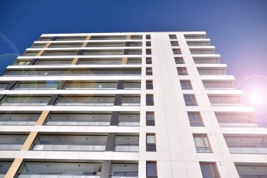 Mavi gökyüzü olan güneşli bir günde modern apartman binaları. Modern bir apartmanın ön cephesi. Güneş ışığıyla kaplı cam yüzey..