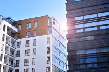 Mavi gökyüzü olan güneşli bir günde modern apartman binaları. Modern bir apartmanın ön cephesi. Güneş ışığıyla kaplı cam yüzey..