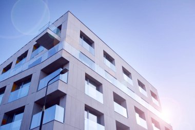 Mavi gökyüzü olan güneşli bir günde modern apartman binaları. Modern bir apartmanın ön cephesi. Güneş ışığıyla cam yüzey.