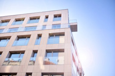 Mavi gökyüzü olan güneşli bir günde modern apartman binaları. Modern bir apartmanın ön cephesi. Güneş ışığıyla cam yüzey.