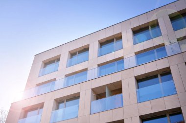 Mavi gökyüzü olan güneşli bir günde modern apartman binaları. Modern bir apartmanın ön cephesi. Güneş ışığıyla cam yüzey.
