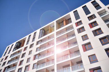 Mavi gökyüzü olan güneşli bir günde modern apartman binaları. Modern bir apartmanın ön cephesi. Güneş ışığıyla cam yüzey.
