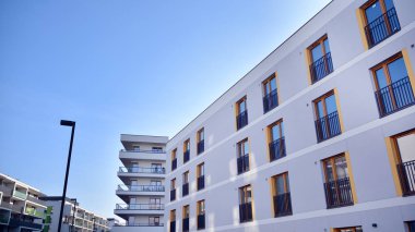Gündüz gözüyle modern yerleşim yerinin dış tarafında. Mavi gökyüzü olan güneşli bir günde modern apartman binaları. Modern bir apartmanın cephesi