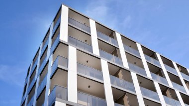 Gündüz gözüyle modern yerleşim yerinin dış tarafında. Mavi gökyüzü olan güneşli bir günde modern apartman binaları. Modern bir apartmanın cephesi