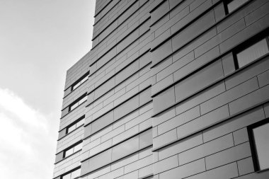 A view at a straight facade of a modern building with a dark grey facade. Dark grey metallic panel facad. Modern architectural details. Black and white.